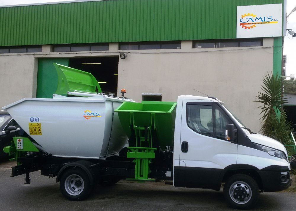 Un camion della spazzatura bianco e verde parcheggiato davanti a un edificio con il tetto verde.