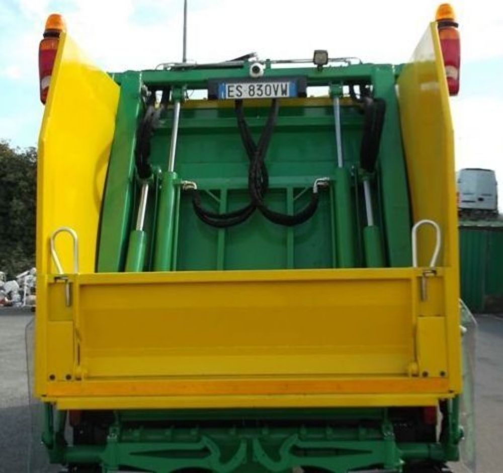 Vista posteriore di un camion della spazzatura verde e giallo con cassone rialzato e bracci idraulici.