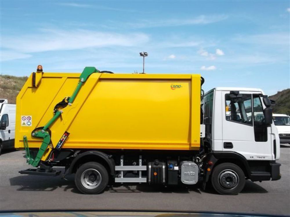 Camion della spazzatura giallo con sollevatore idraulico verde parcheggiato su una strada sotto un cielo azzurro