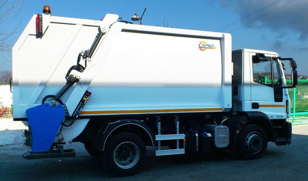 Camion della spazzatura bianco con vano posteriore e braccio laterale blu, parcheggiato all'aperto al crepuscolo.