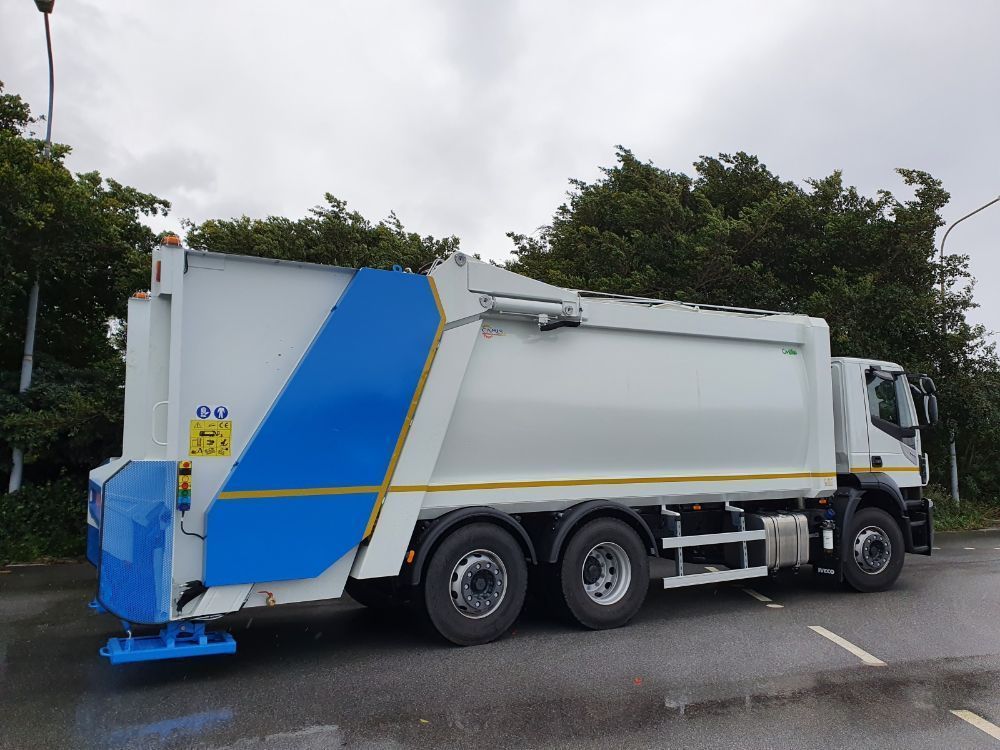 Camion della spazzatura bianco con una striscia blu parcheggiato su una strada vicino agli alberi.