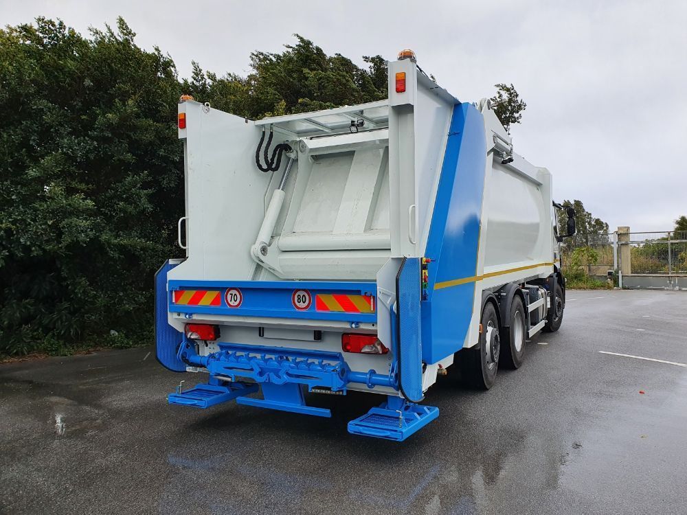 Vista posteriore di un camion della spazzatura blu e bianco parcheggiato su una strada bagnata vicino agli alberi.