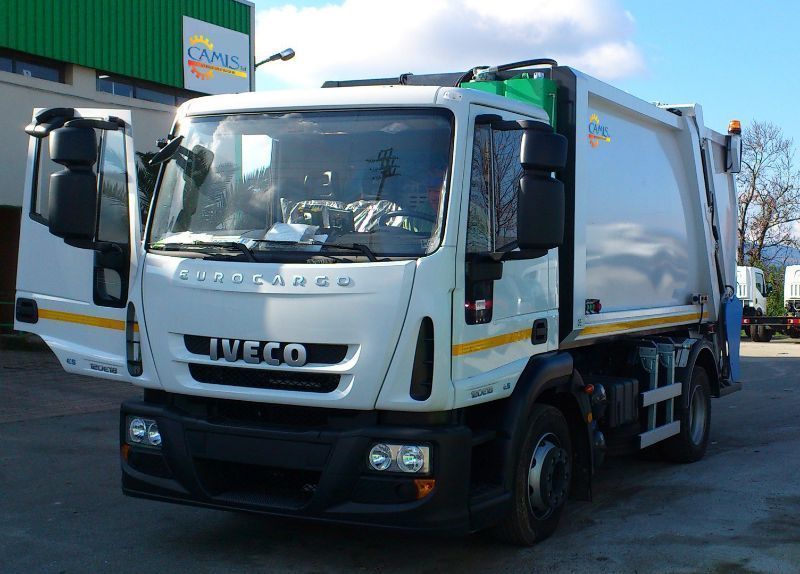 Camion furgonato Iveco bianco parcheggiato all'aperto su una strada soleggiata, vista frontale.