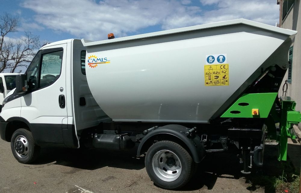 Camion bianco per la raccolta dei rifiuti con attrezzatura posteriore verde parcheggiato all'aperto sotto un cielo azzurro.