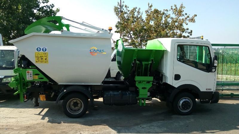 Camion betoniera bianco e verde parcheggiato all'aperto vicino agli alberi, in pieno giorno.