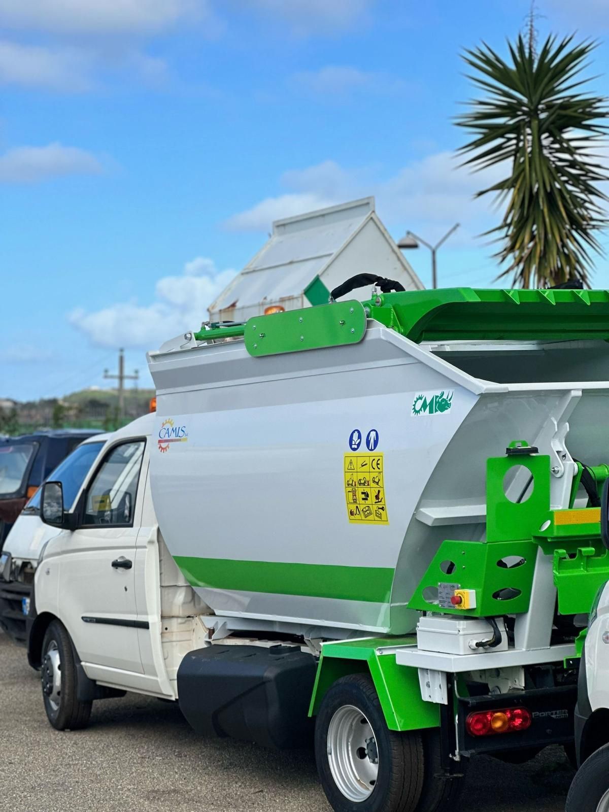 Camion bianco con rimorchio per la spazzatura verde parcheggiato all'aperto sotto un cielo azzurro.