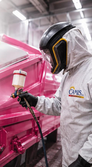 Un operaio con tuta protettiva vernicia a spruzzo un macchinario rosa in un'officina.