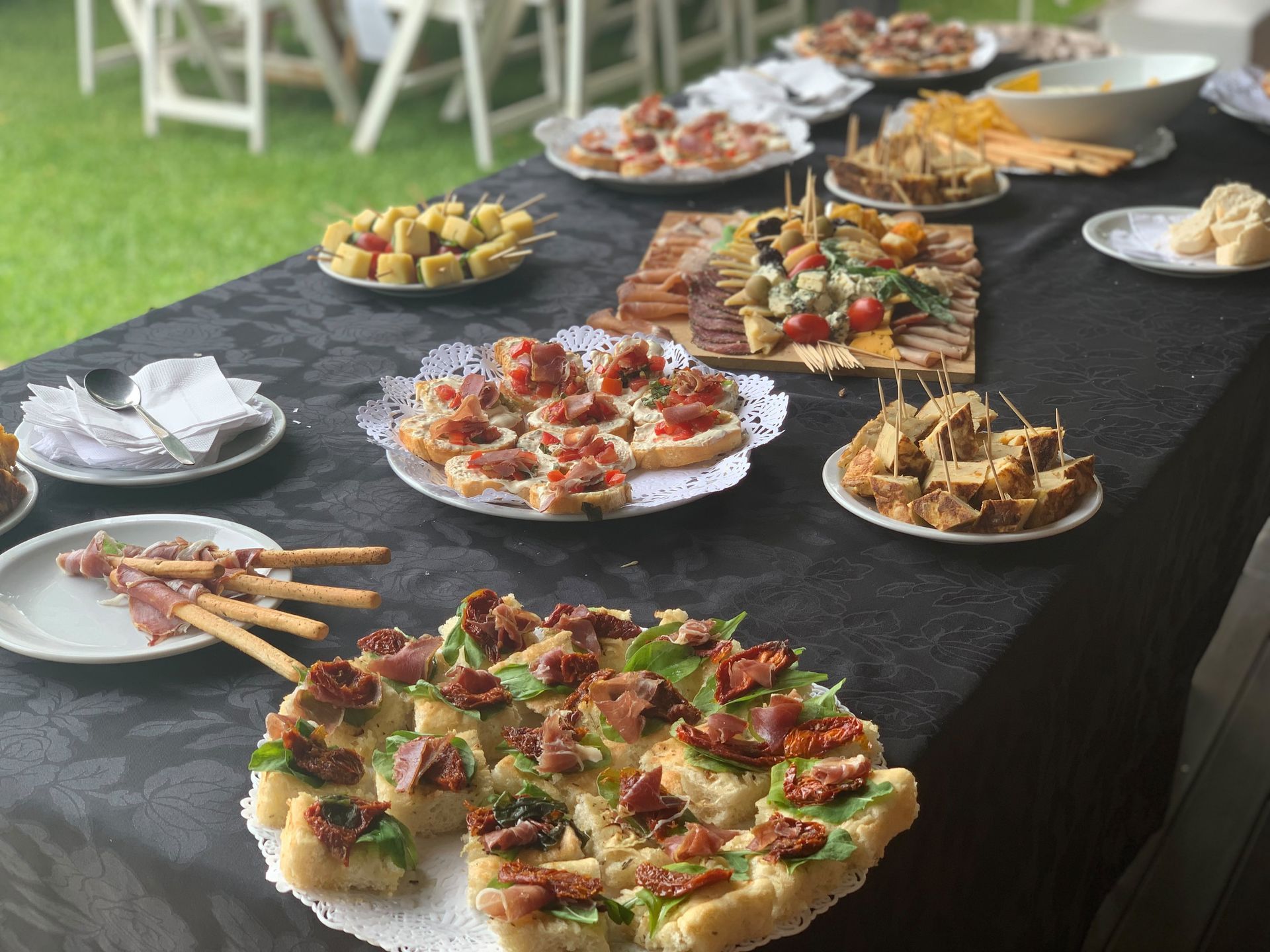Mesa de bufé con una selección de aperitivos en bandejas y brochetas en un evento al aire libre