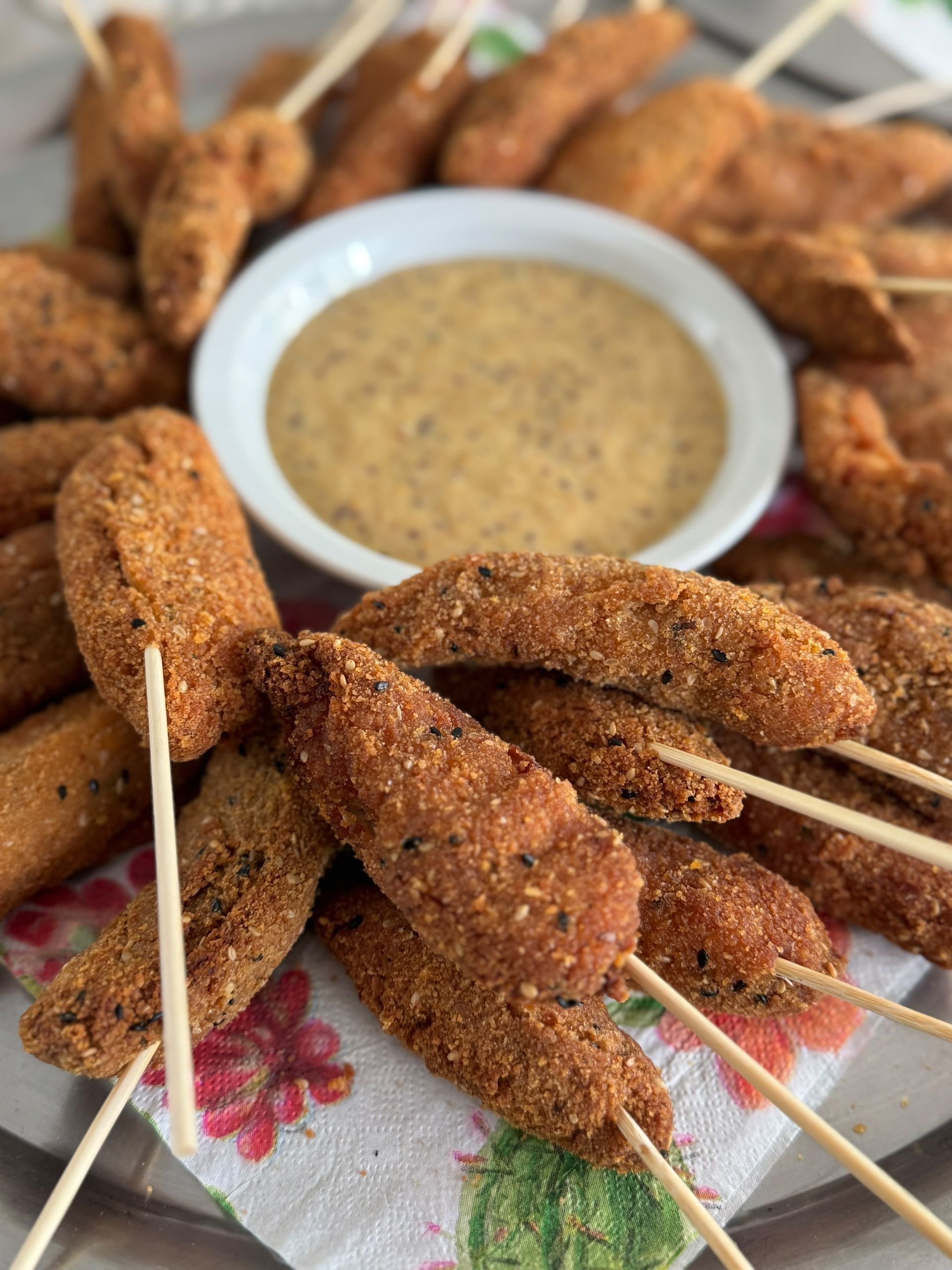 Brochetas empanadas con salsa para mojar sobre un mantel floral