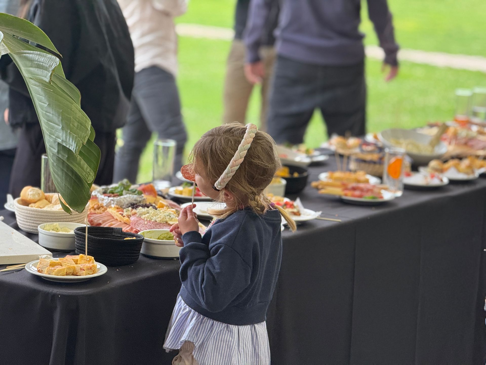 Niño intentando alcanzar comida en una mesa de bufé al aire libre durante una reunión