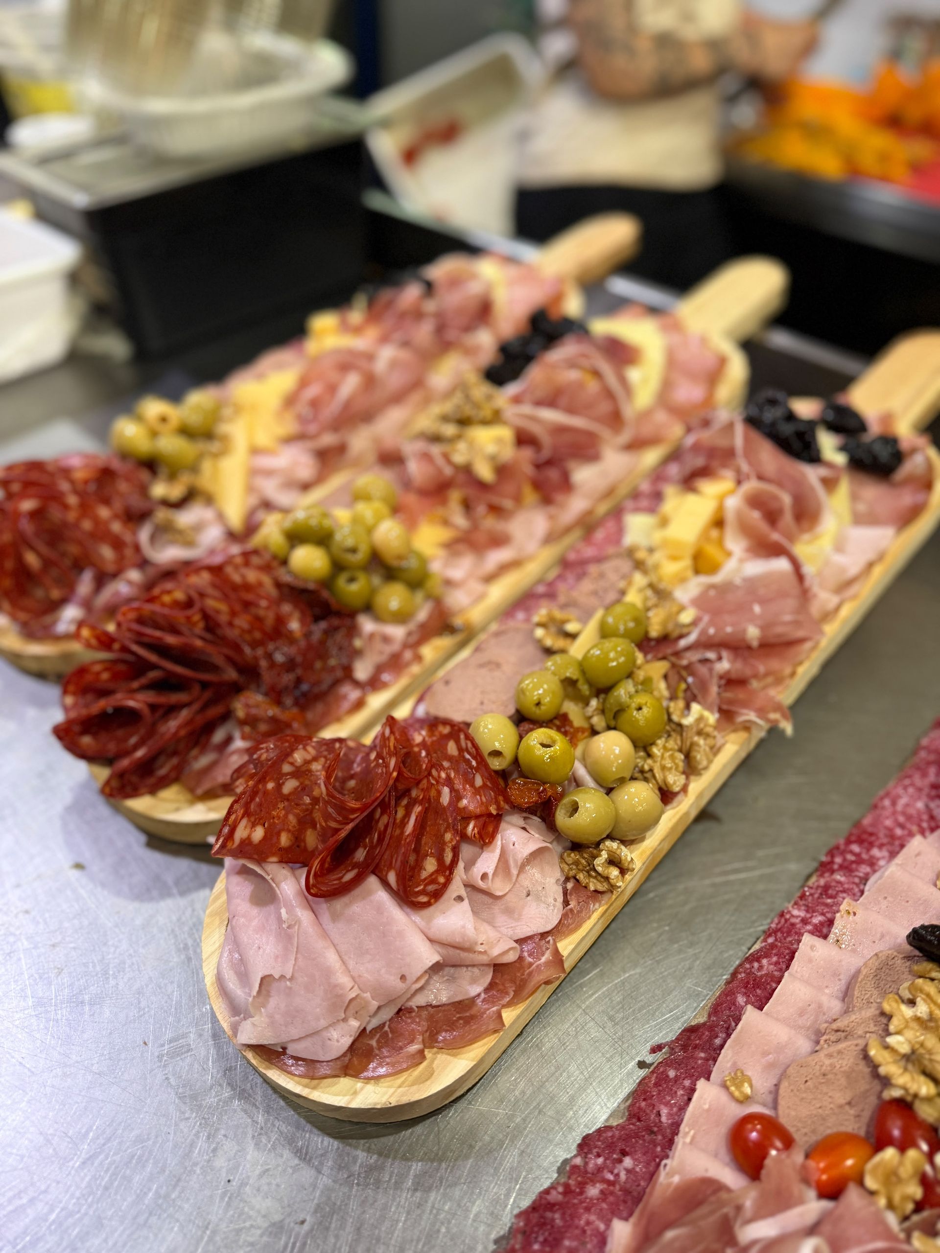 Variedad de sándwiches abiertos con carnes, aceitunas y tomates en el mostrador de una charcutería