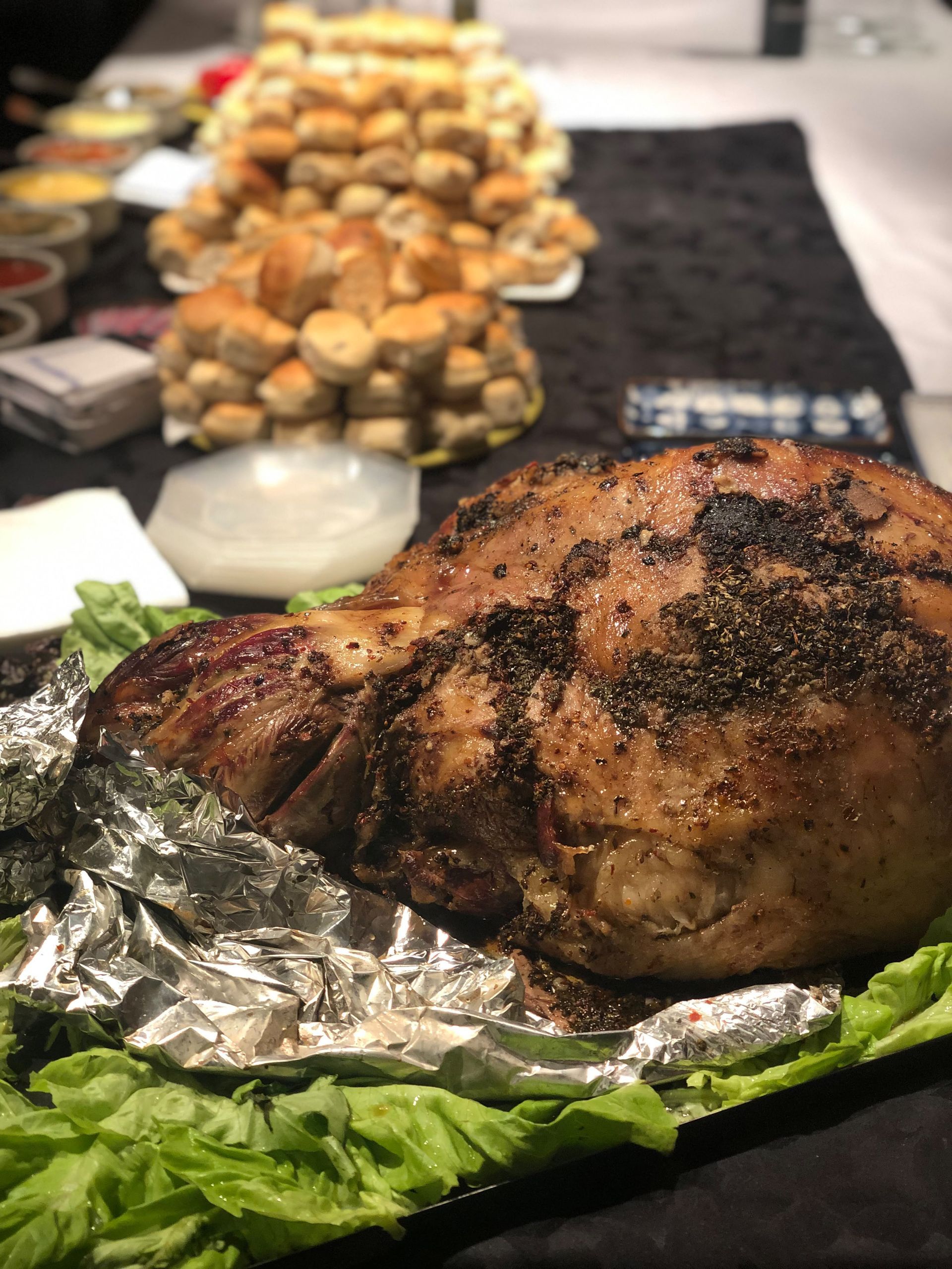 Pavo asado en una bandeja cubierta con papel de aluminio, acompañado de verduras de hoja verde y servido junto a cuencos con guarniciones en un bufé