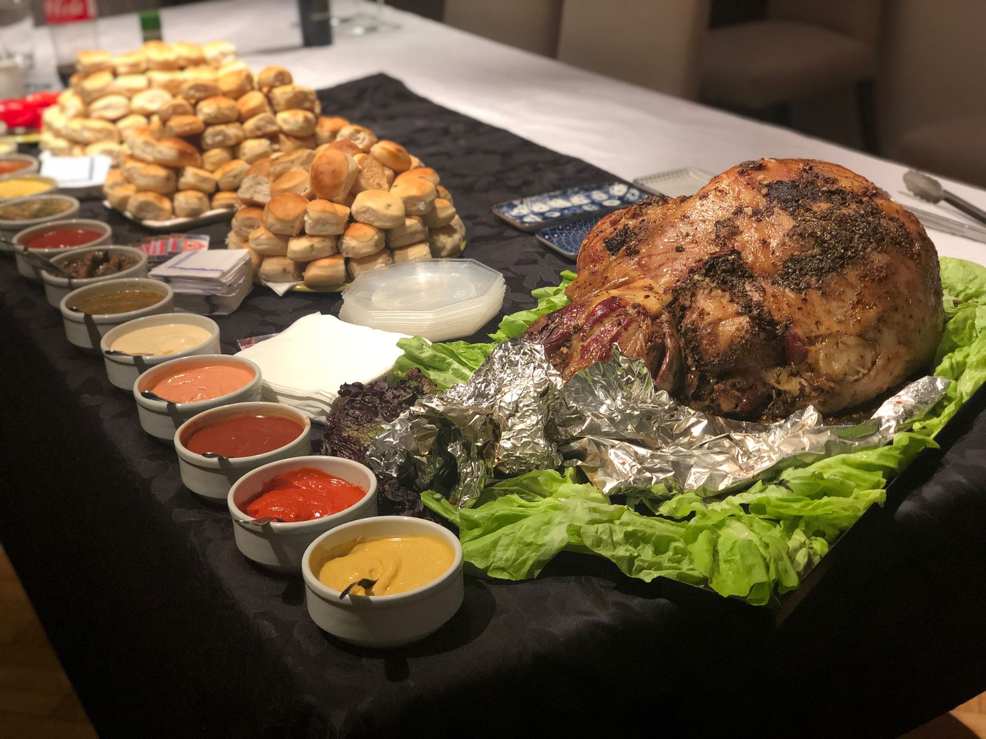 Mesa de buffet con un cerdo asado, carne trinchada y una variedad de salsas sobre un mantel negro.