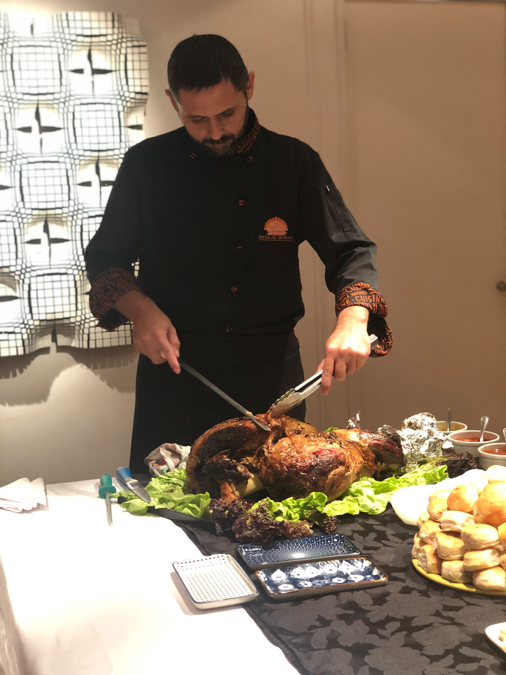 Una persona trincha un asado en una mesa de bufé con verduras, patatas y fuentes para servir