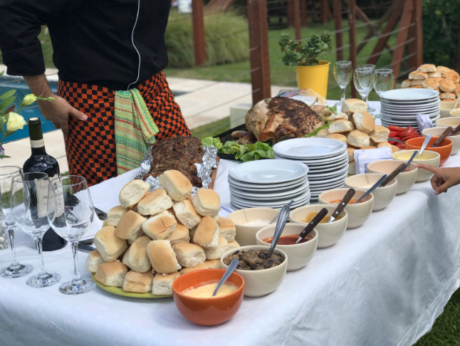 Mesa de bufé al aire libre con pan, embutidos en lonchas, cuencos de salsas y platos apilados en una reunión en el jardín