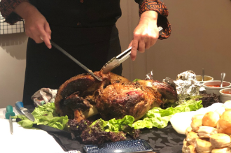 Una persona trincha un pavo asado en una mesa con ensalada, panecillos y guarniciones