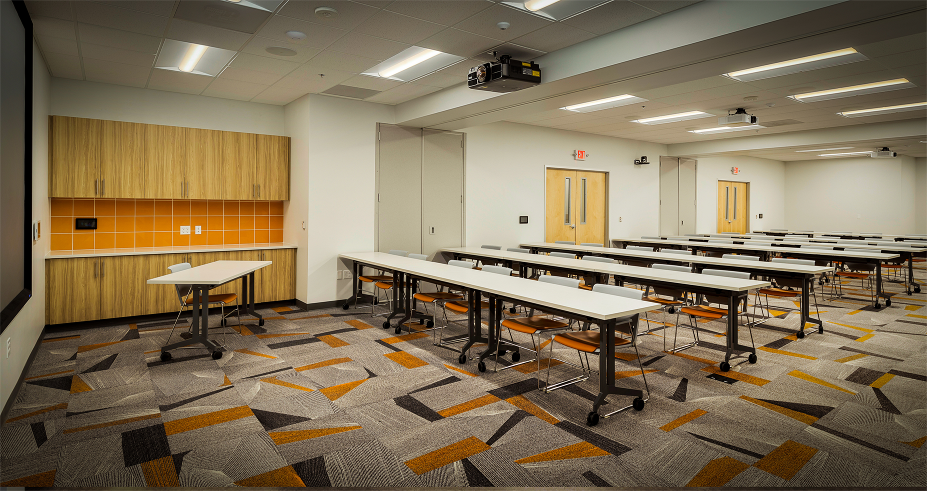 A large room with tables and chairs and a projector on the ceiling.
