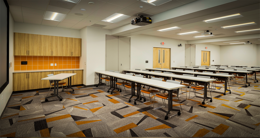 A large room with tables and chairs and a projector on the ceiling.