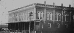 Black and white photograph of a two-story brick building with a covered walkway and tall windows.
