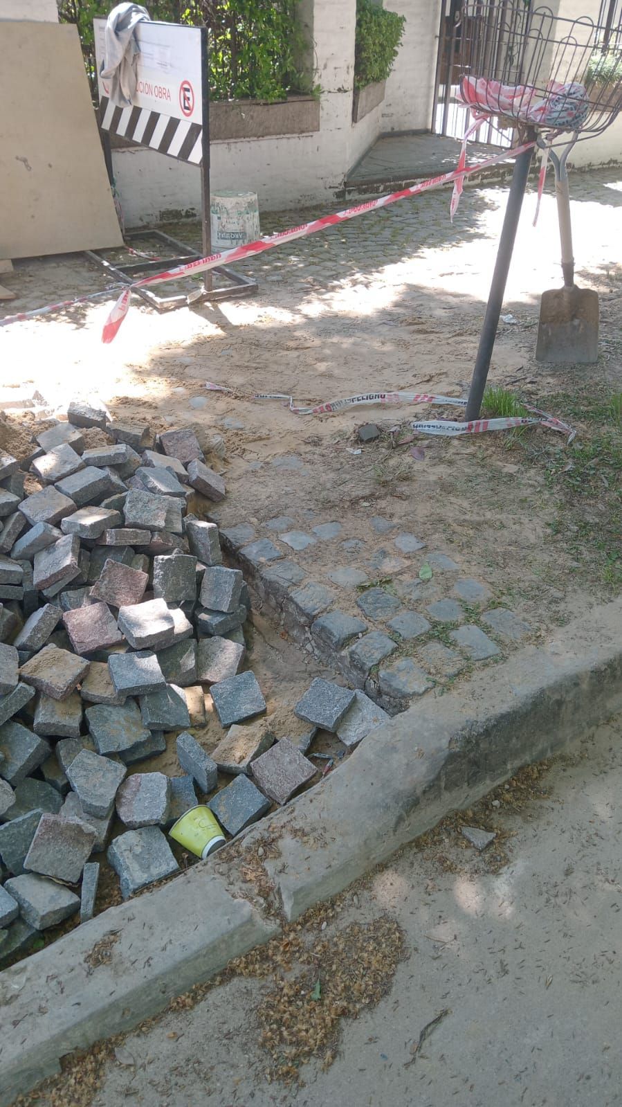 Escombros de construcción junto a una acera, con cinta roja de precaución que delimita una pequeña zona de trabajo.