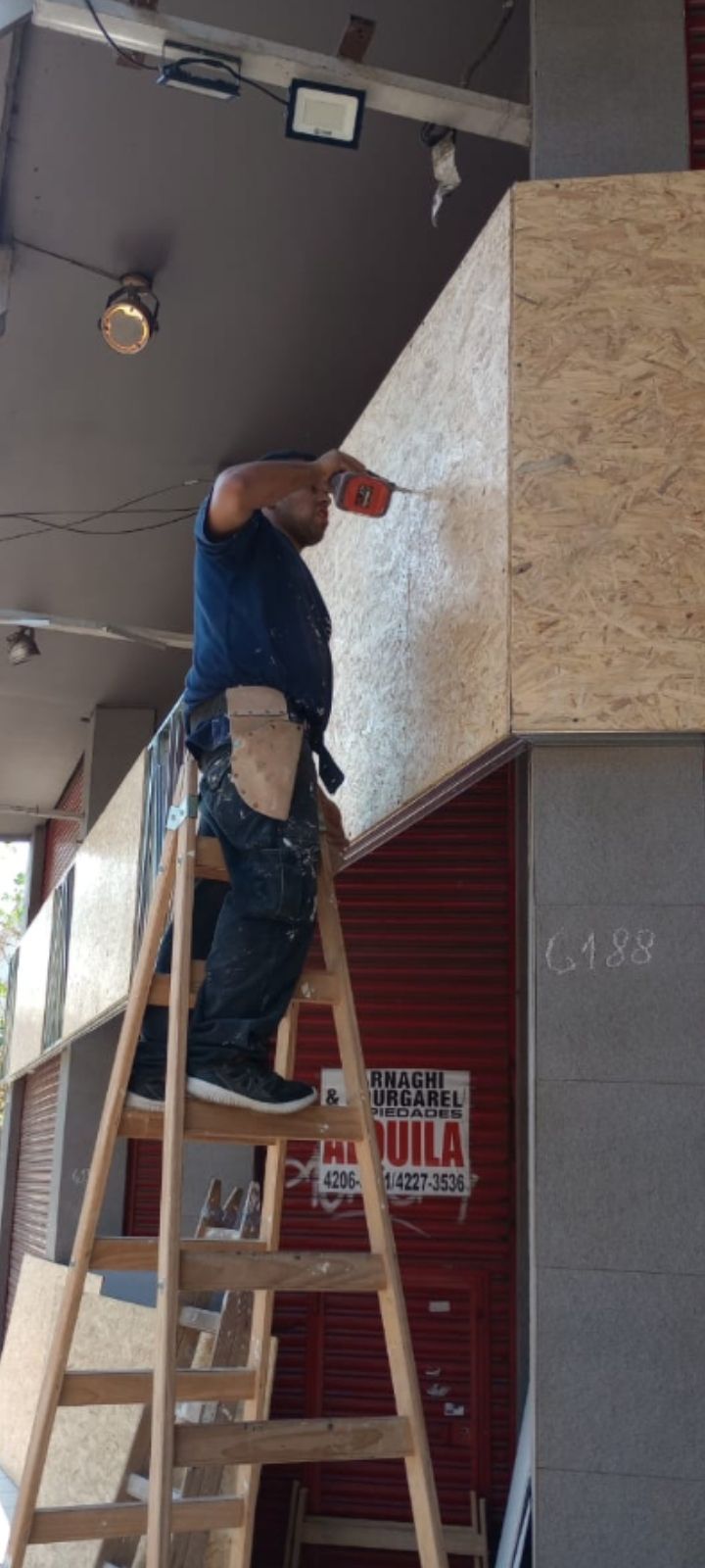 Un trabajador subido a una escalera instala un panel de madera en el techo, en el exterior de una tienda.