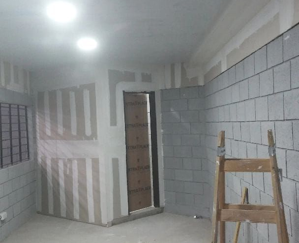 Habitación parcialmente terminada con paredes alicatadas, luces en el techo y una escalera cerca de una puerta.