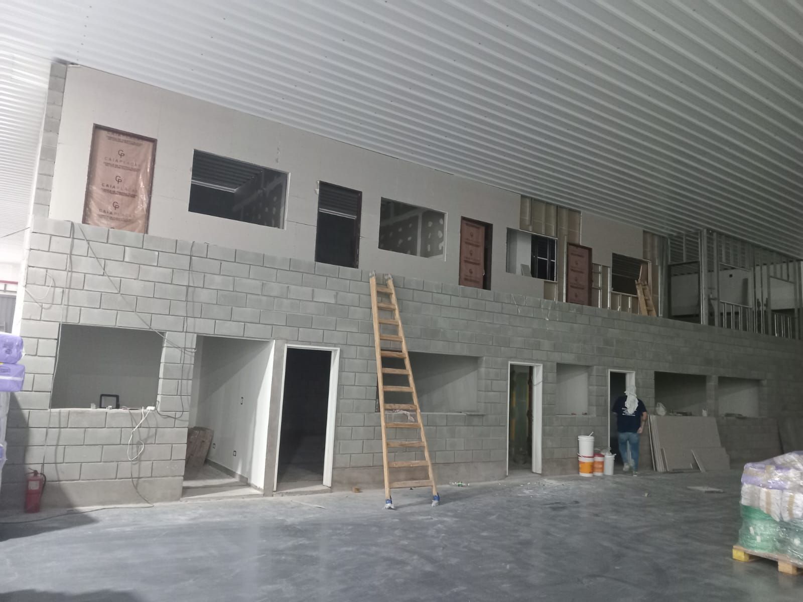 Obra en construcción interior con paredes de bloques de hormigón, puertas abiertas, una escalera y materiales apilados.