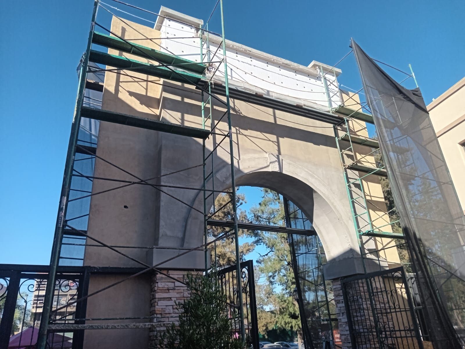 Andamios alrededor de la entrada de un edificio en construcción, con una abertura arqueada y cielo azul arriba.