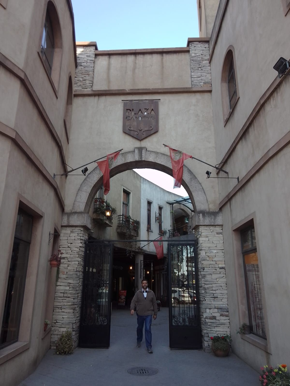 Un estrecho arco de piedra da a una calle, con banderas rojas y una persona que camina por el pasaje.