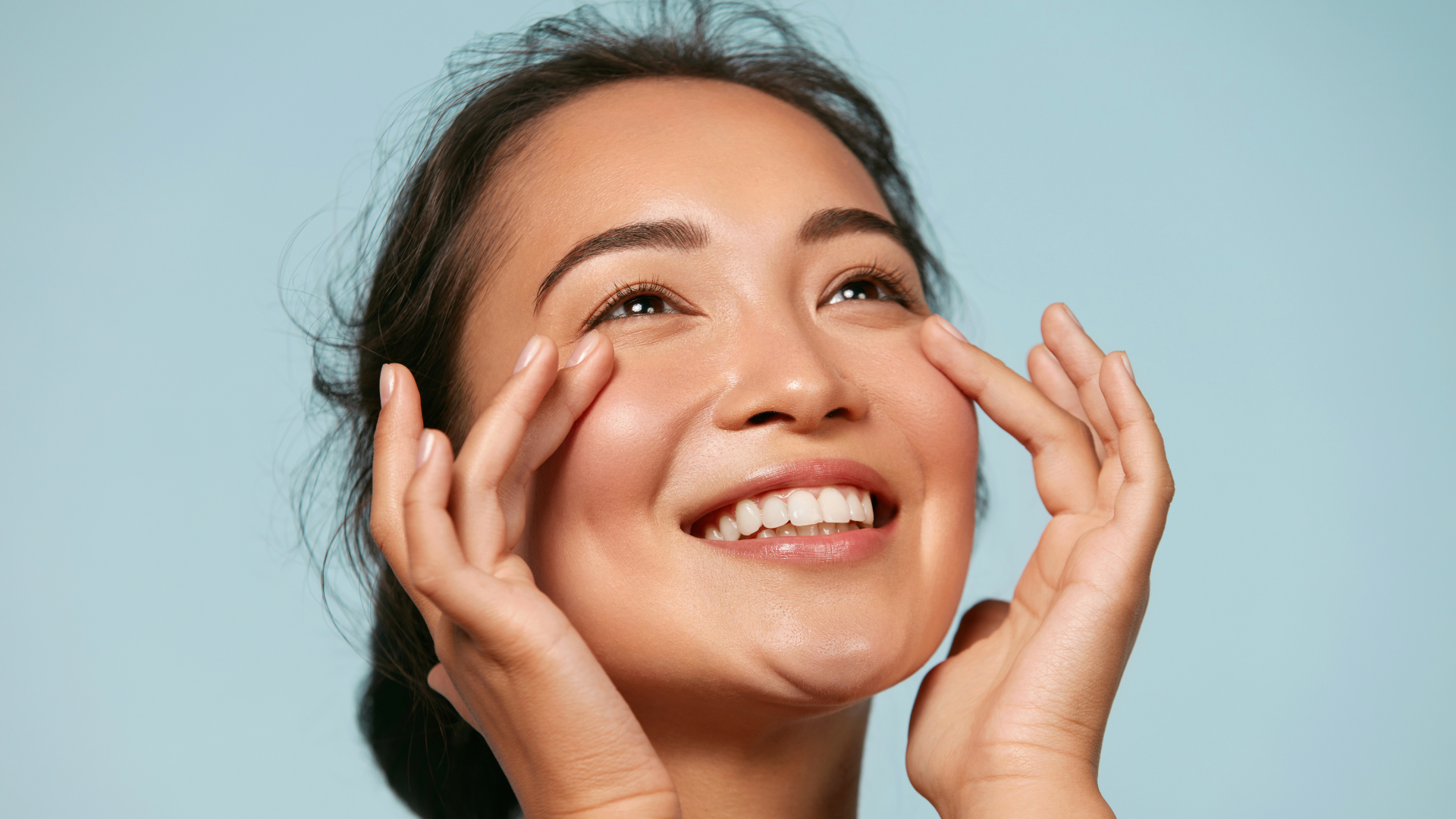 Smiling woman touching her face against a light blue background