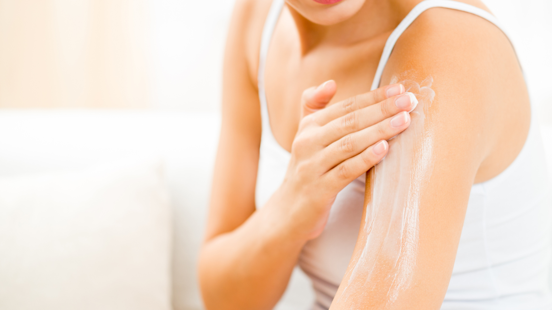 Person applying white lotion to shoulder and upper arm in bright bathroom