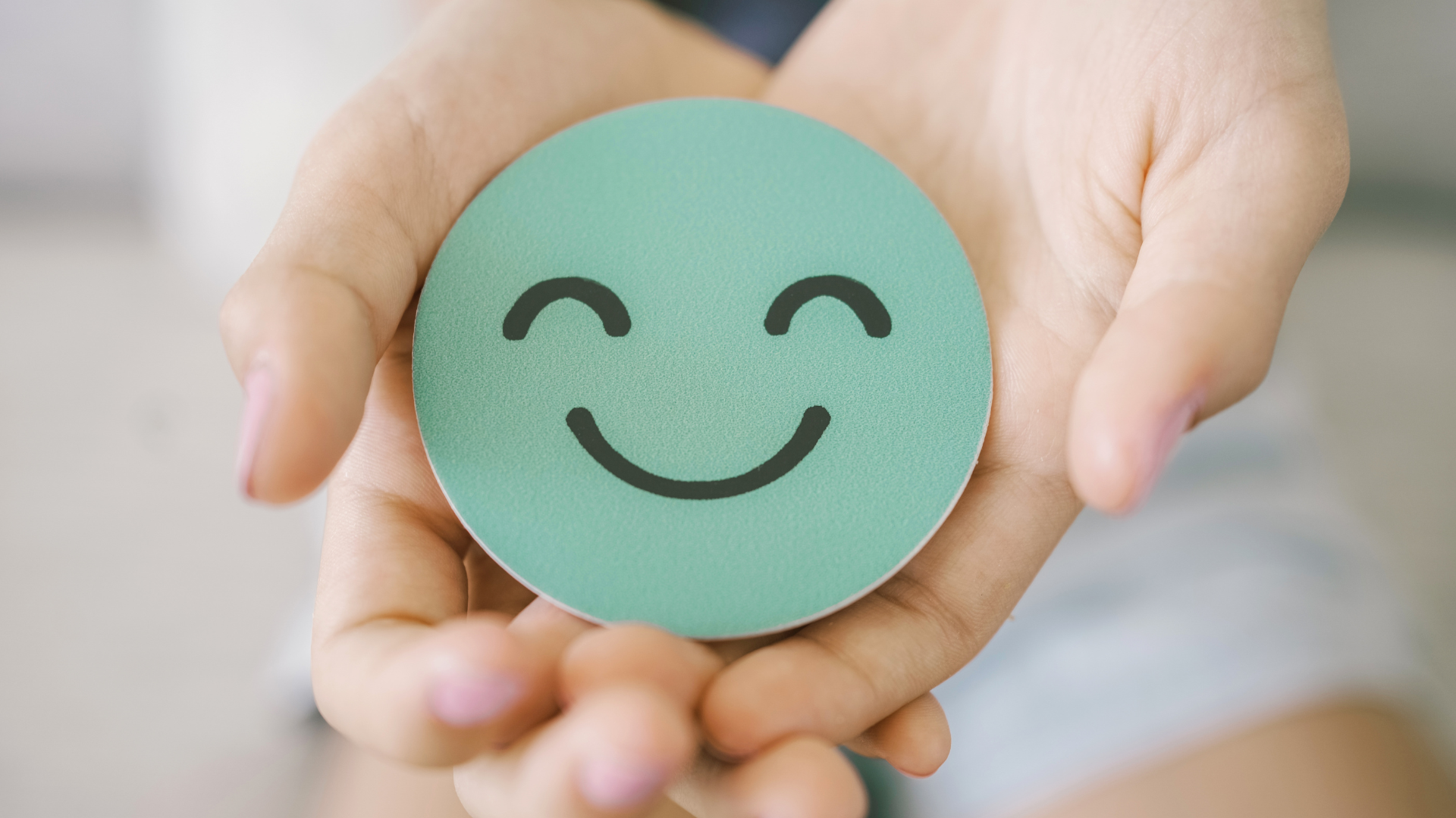 Hands holding a teal smiley face button with a simple black smiling expression.