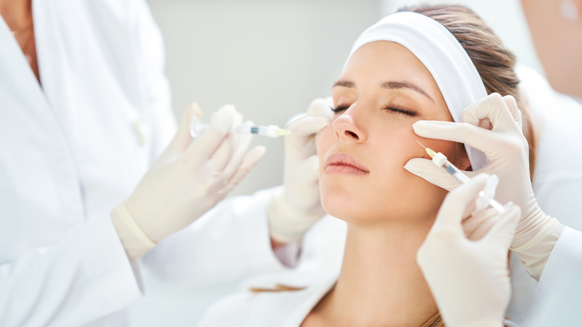 Cosmetic treatment on woman’s face with gloved practitioners applying cream in a bright spa clinic