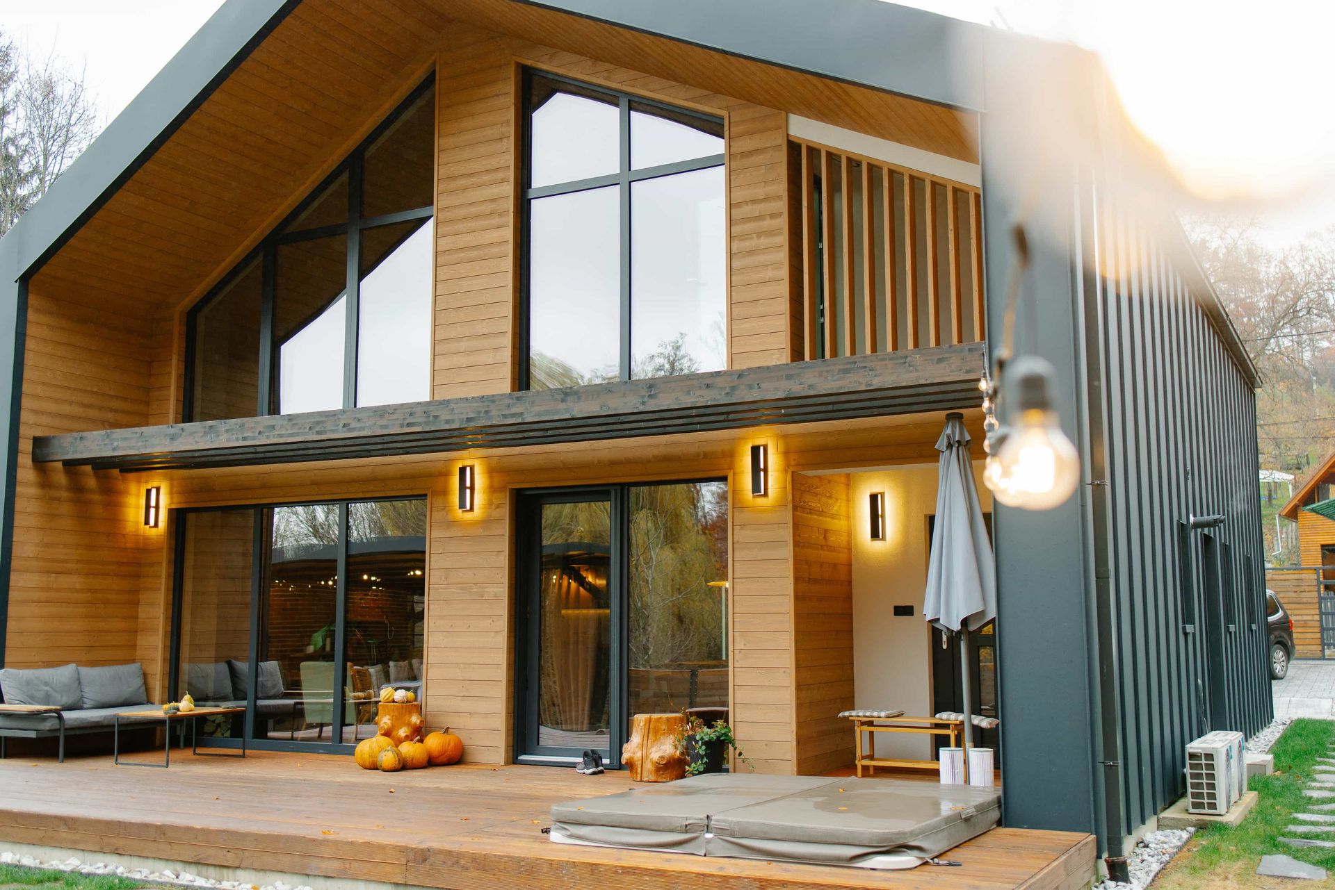 Modern wooden house with large windows, patio, and outdoor lighting.
