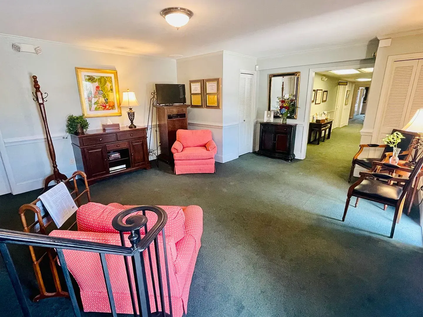 Bright living room with green carpet, pink armchairs, wood furniture, and an open doorway to a dining area