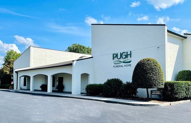 Pugh building exterior with white stucco walls, arched entrance, and manicured shrubs under a blue sky