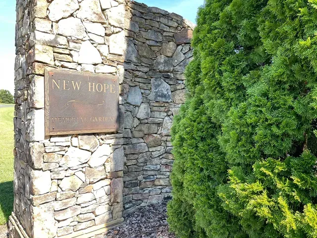 Stone wall sign reading “New Hope” beside a dense green shrub.