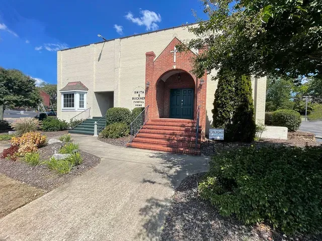 Brick entrance on a beige building with red steps, blue door, and surrounding shrubs under a sunny sky