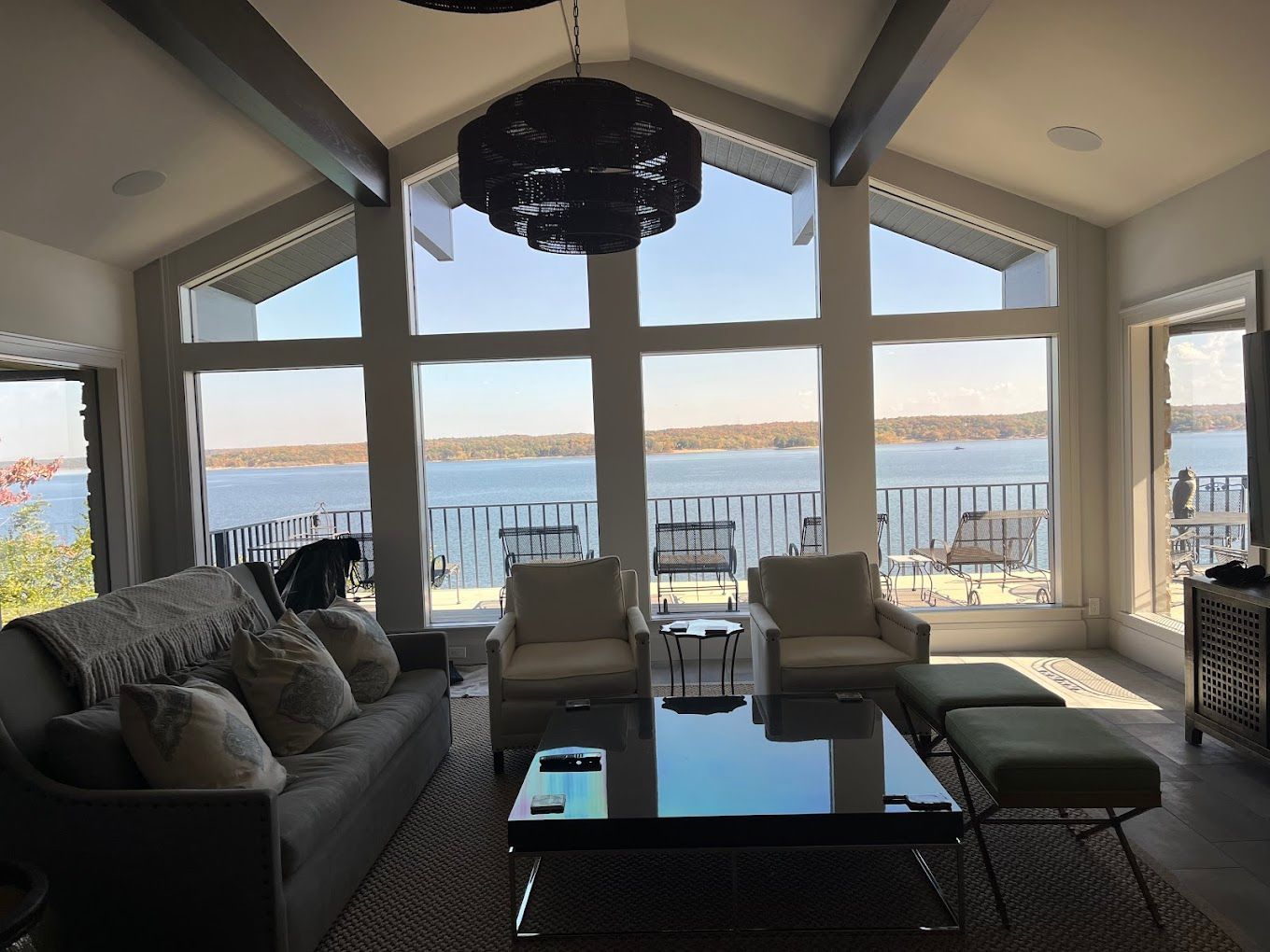 Living room with large windows overlooking a lake. Gray sofa, armchairs, and a black coffee table.