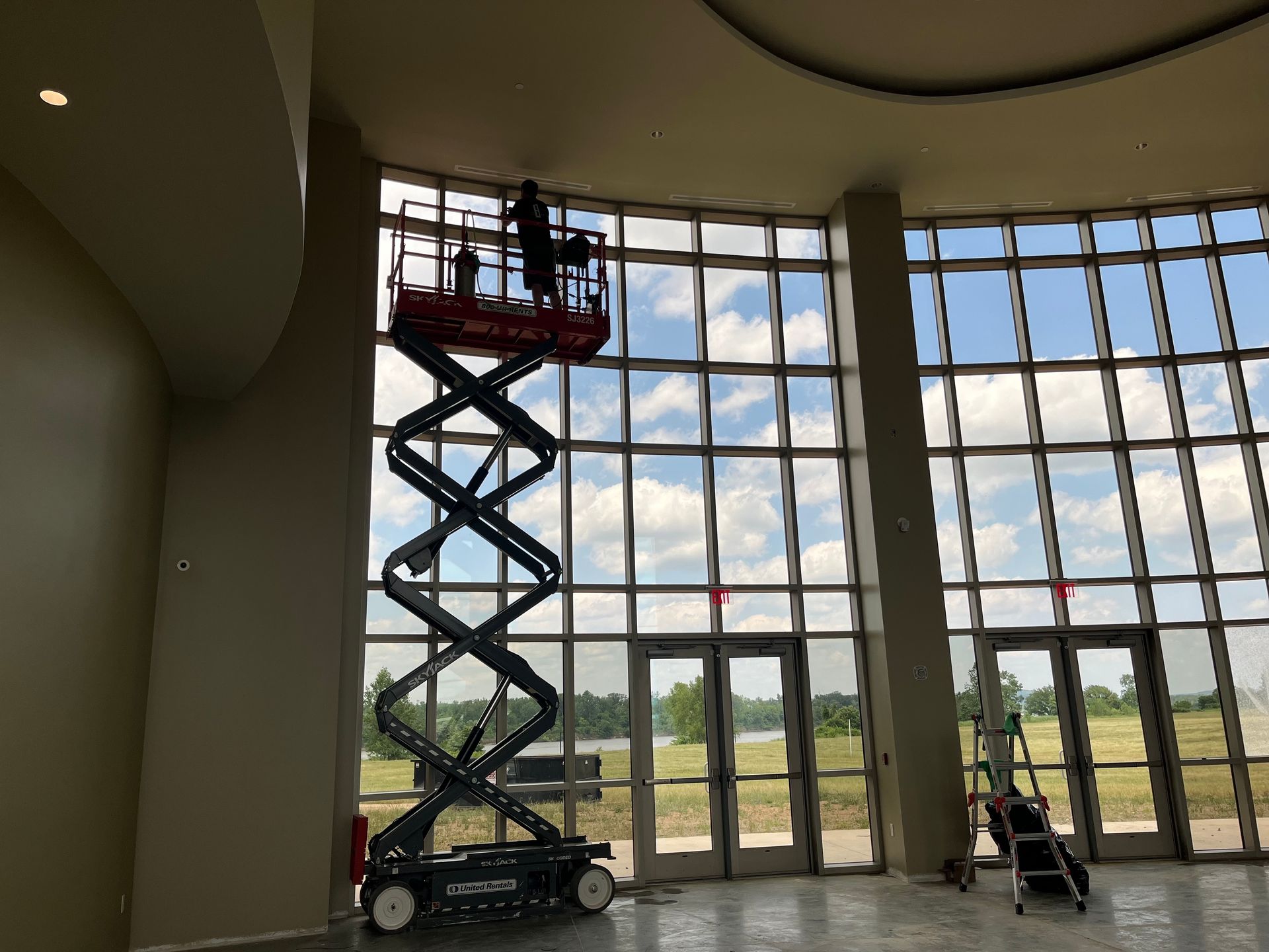 Person on a scissor lift working on interior windows of a building. Sunny day, clear sky.