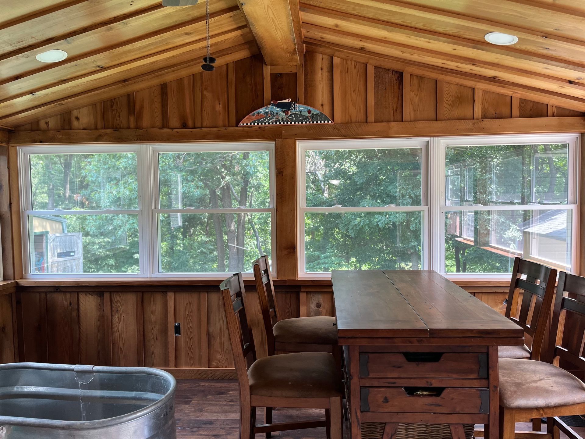 Enclosed porch with wood paneling, windows, table and chairs, and a metal tub.