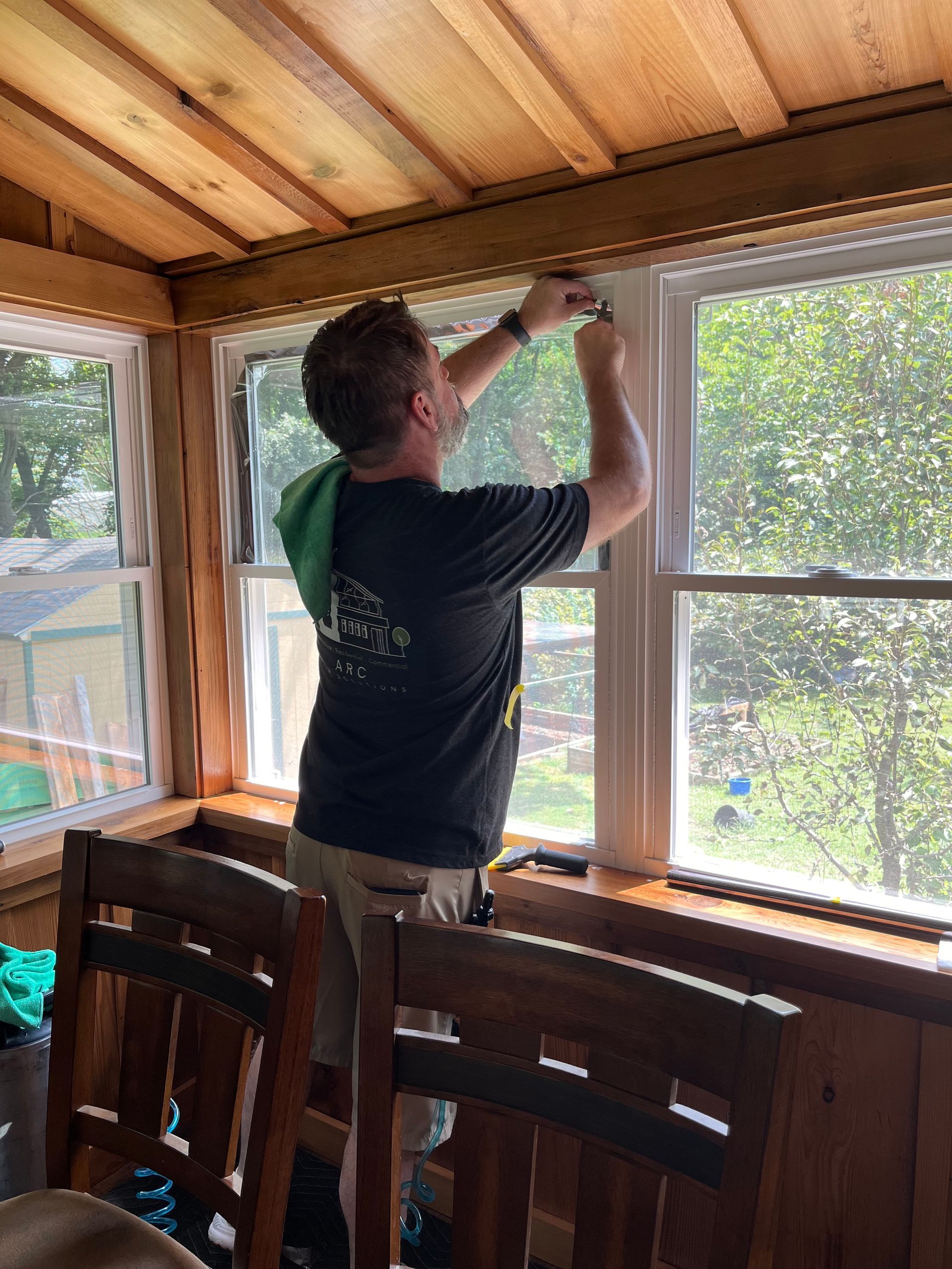 Man cleaning a window inside a room with wooden paneling, using a squeegee.