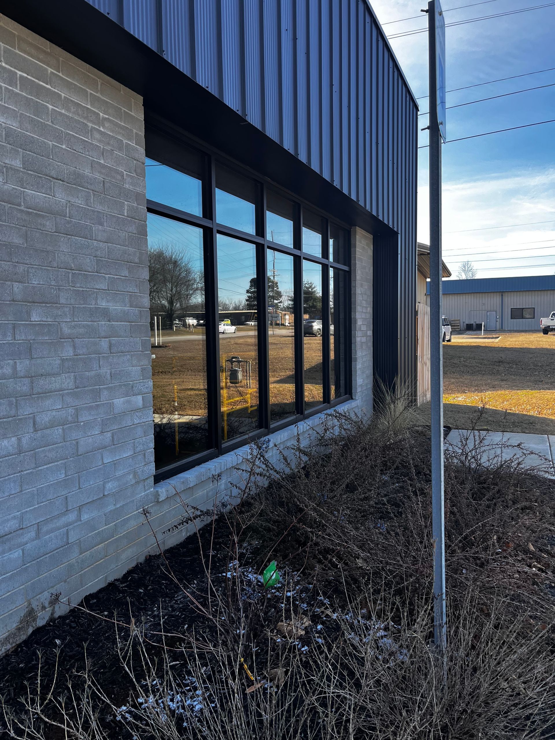 Building exterior with black-framed windows reflecting the outside. Brick wall and dark metal siding.