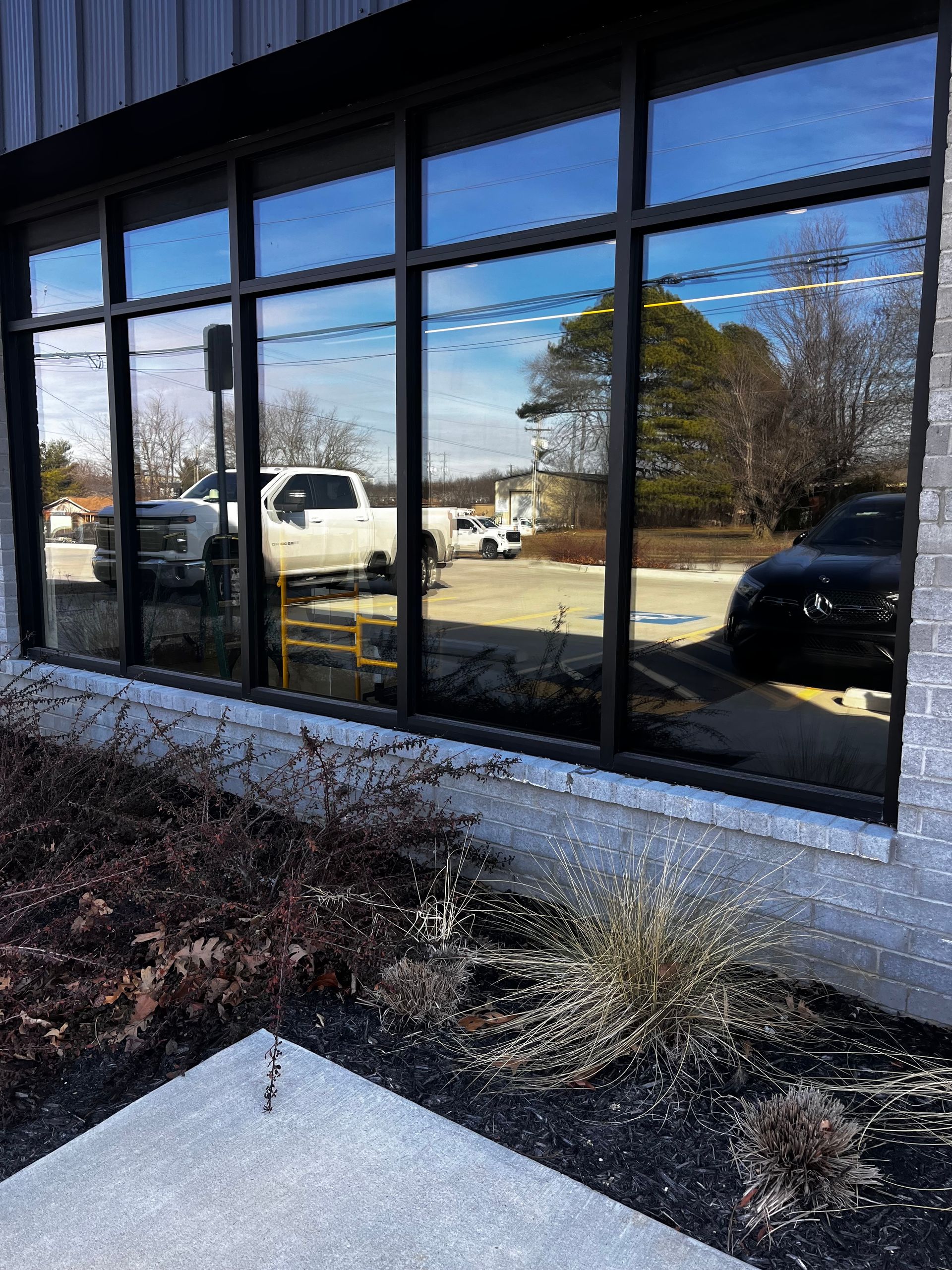 Reflective glass window of a building with parked vehicles and landscaping.