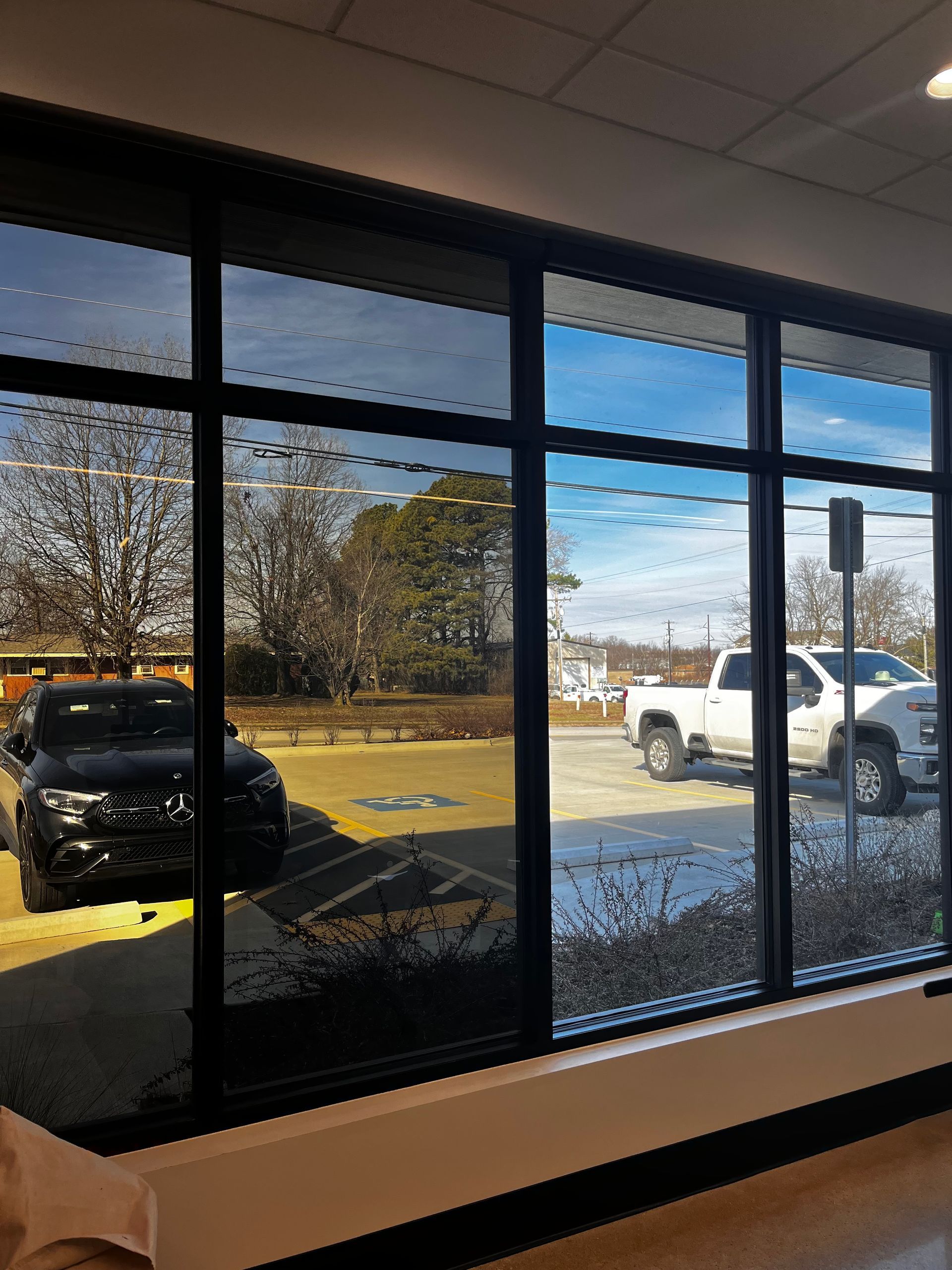 Exterior view through large windows: cars parked outside, sunny blue sky, trees.
