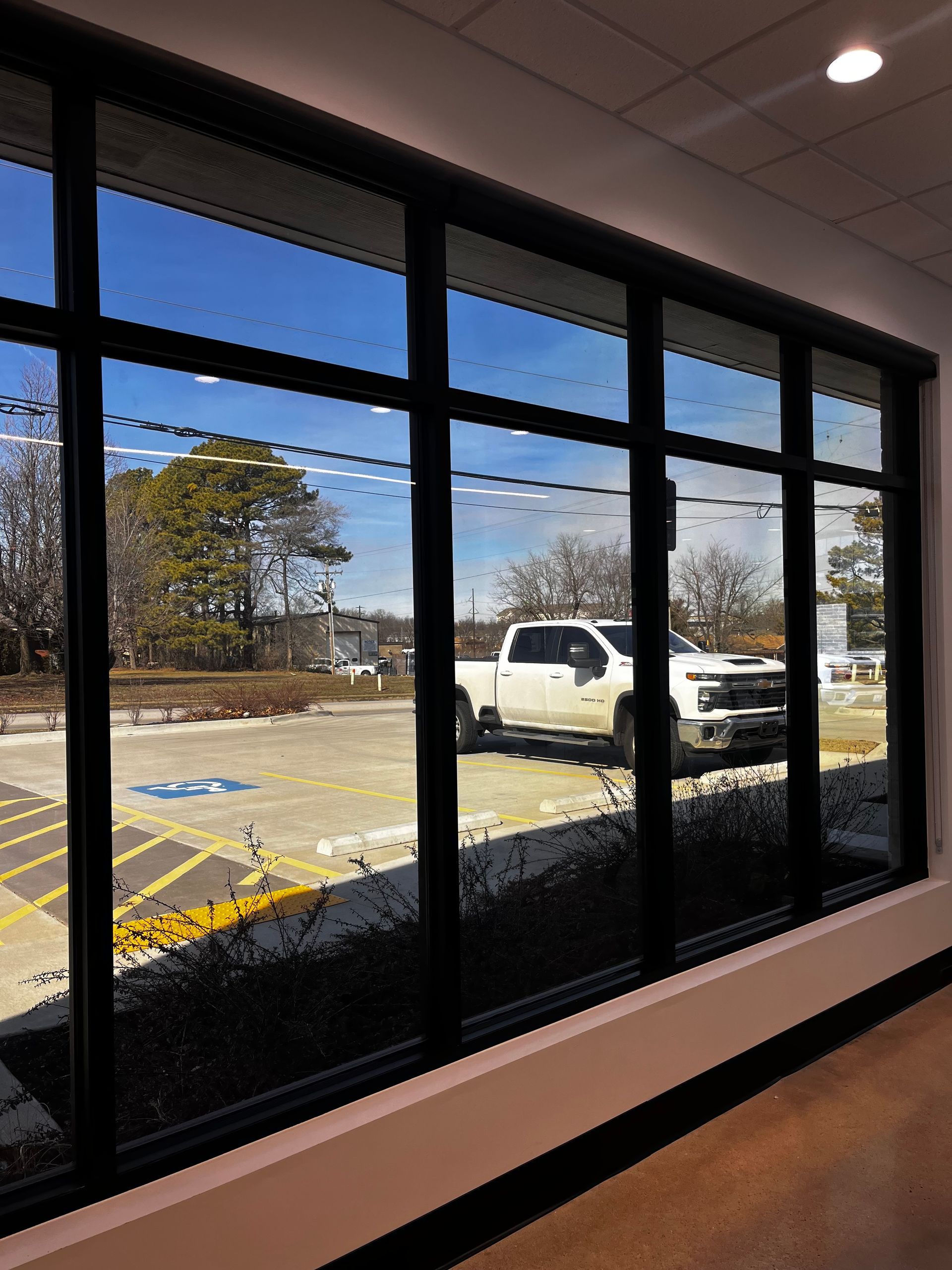 Large window with black frames overlooking parking lot and a white truck on a sunny day.