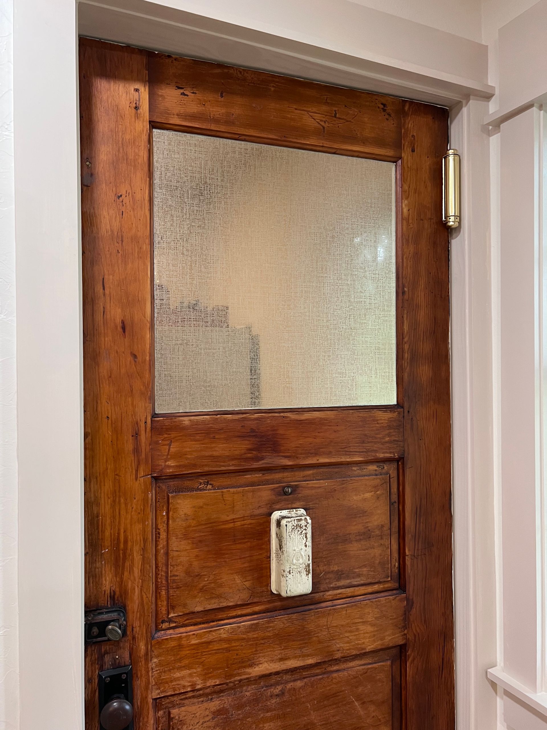 Wooden door with textured glass panel, white trim, and a white, aged door handle.