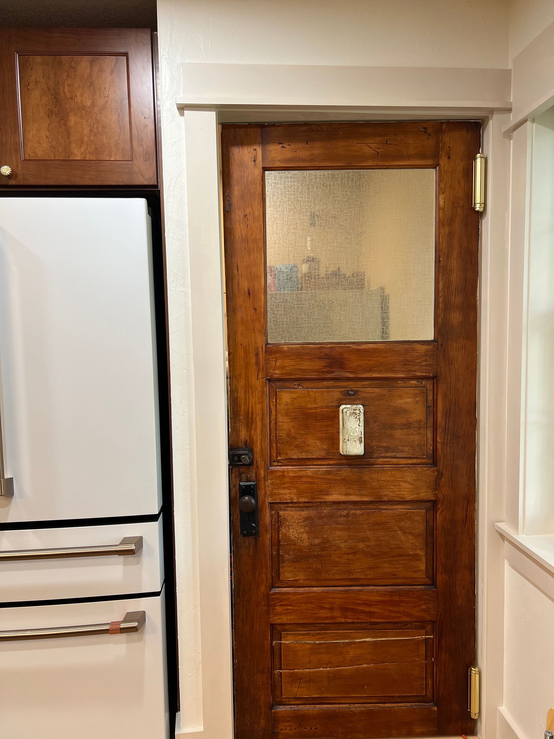 Wooden door with frosted glass panel and white trim, next to a white refrigerator with stainless steel handles.