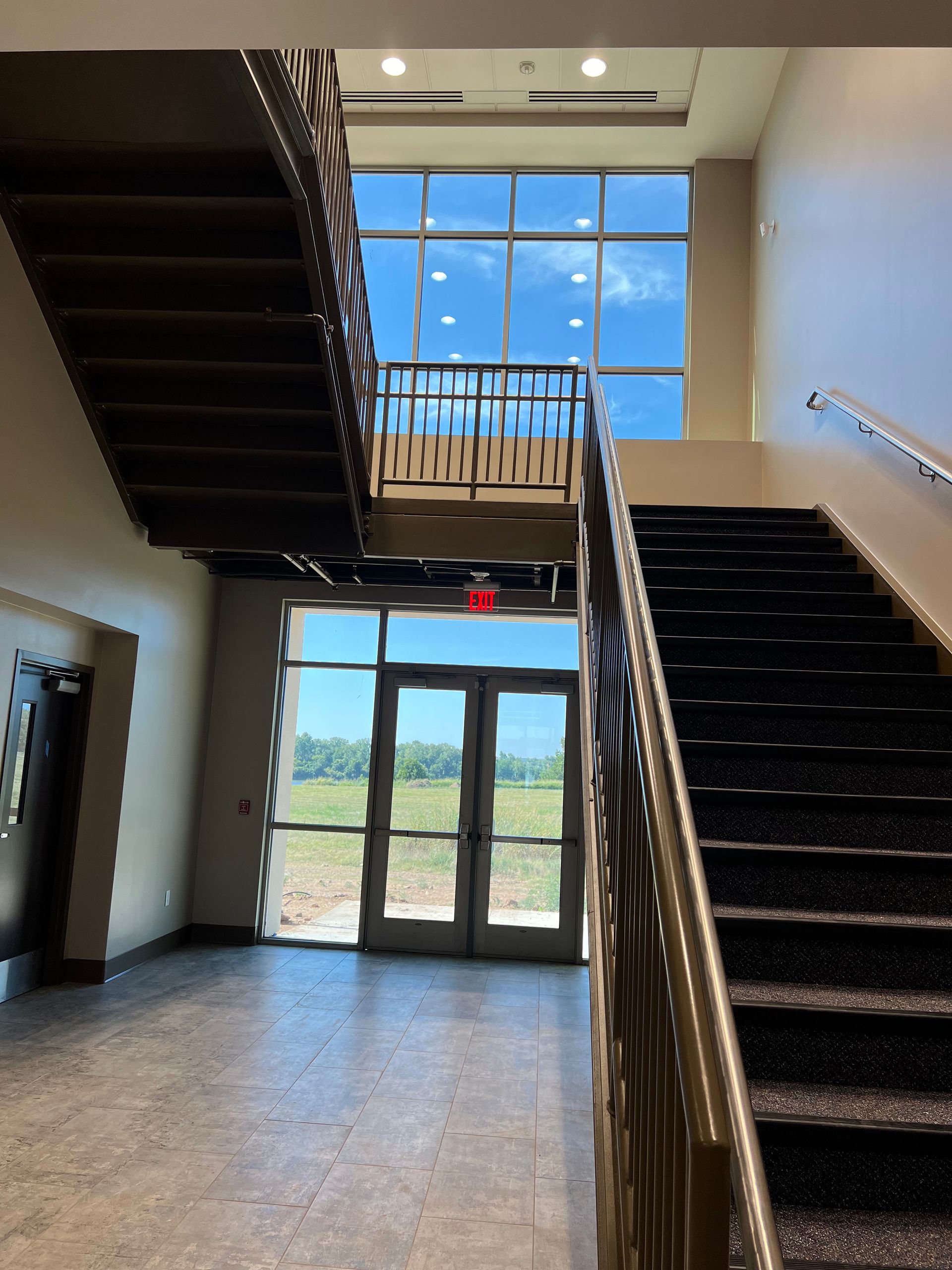 Interior view with two staircases, glass doors and large windows with blue sky visible.