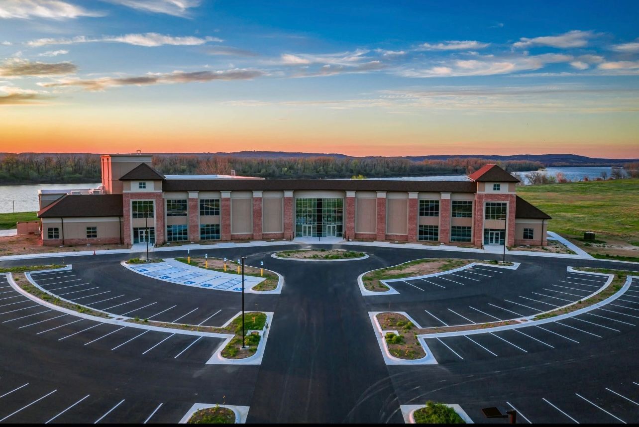 Large brick building with a large parking lot. Sky is blue with sunset colors in background.